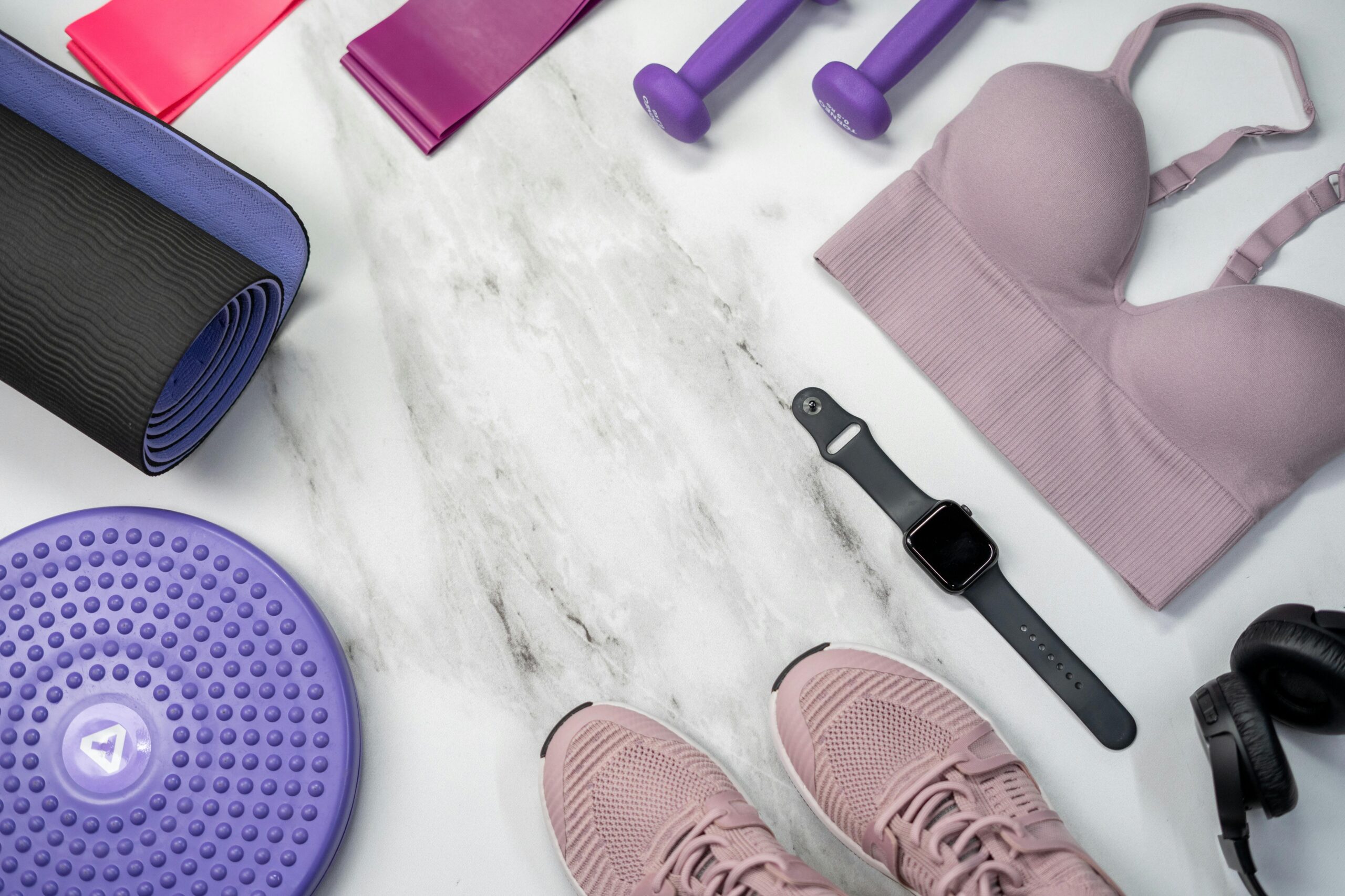 Yoga mat, smart watch, dumbbells, sport shoes, and yoga straps arranged for a workout.