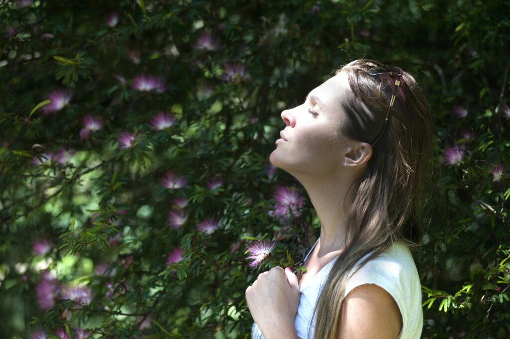 A girl standing next to a lush green plant wall, enjoying the sunshine with a serene expression.