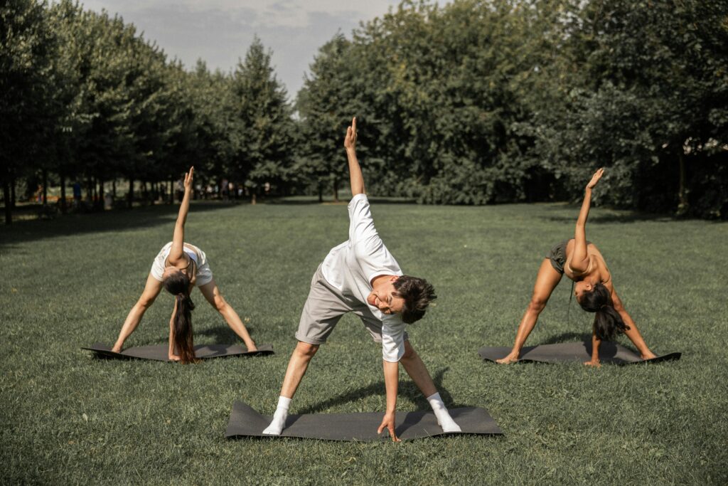 Three people practicing yoga on the grass, enjoying an outdoor session.