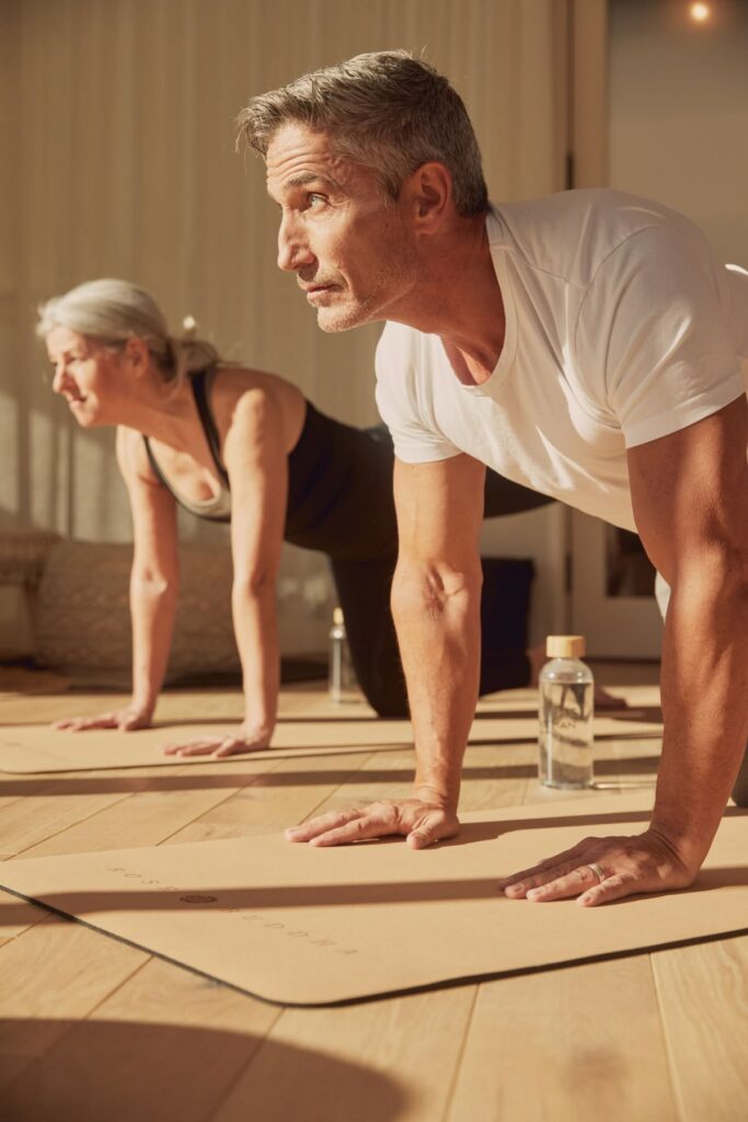 Two adults engaging in a cardio workout. Both in a position to do push ups.