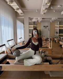 Woman wearing stylish Pilates workout clothing sitting on a Reformer in a Pilates studio