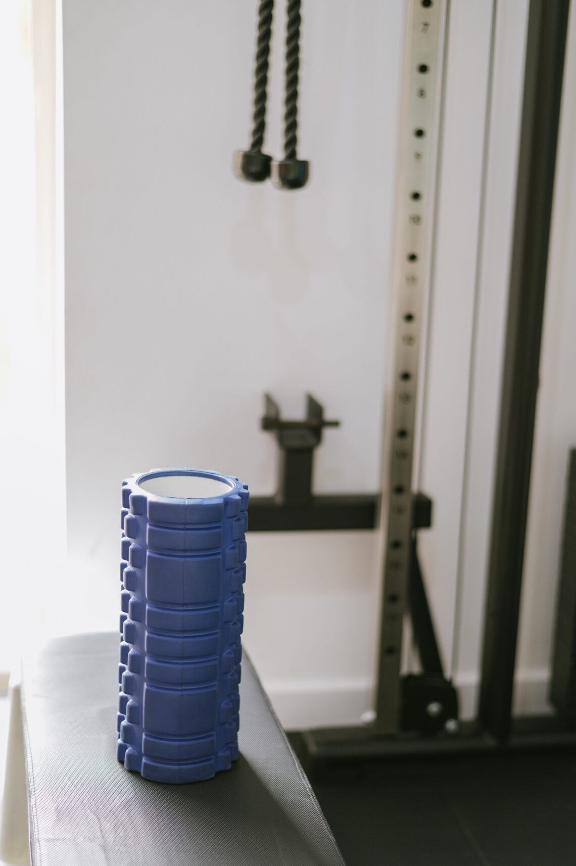 A blue muscle roller used in post workout recovery sits on a bench in a contemporary gym, highlighting fitness equipment.