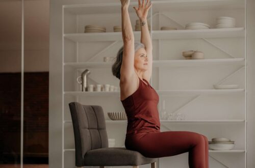 woman practicing gentle yoga position on chair in a light background demonstrating flexibility with raised hands